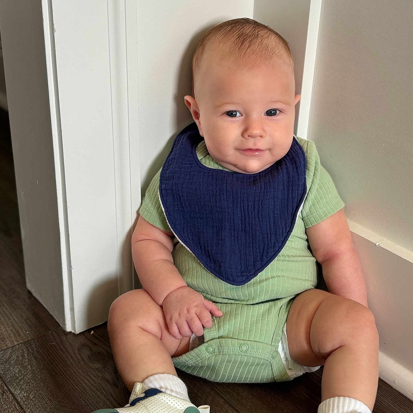Cam joined the competition — help win amazing prizes! baby, child, infant, sitting, onesie, bib, sneakers, floor, wooden_floor, wall, indoors, cute, smile, face, head, footwear, person, young, casual_clothing, happy