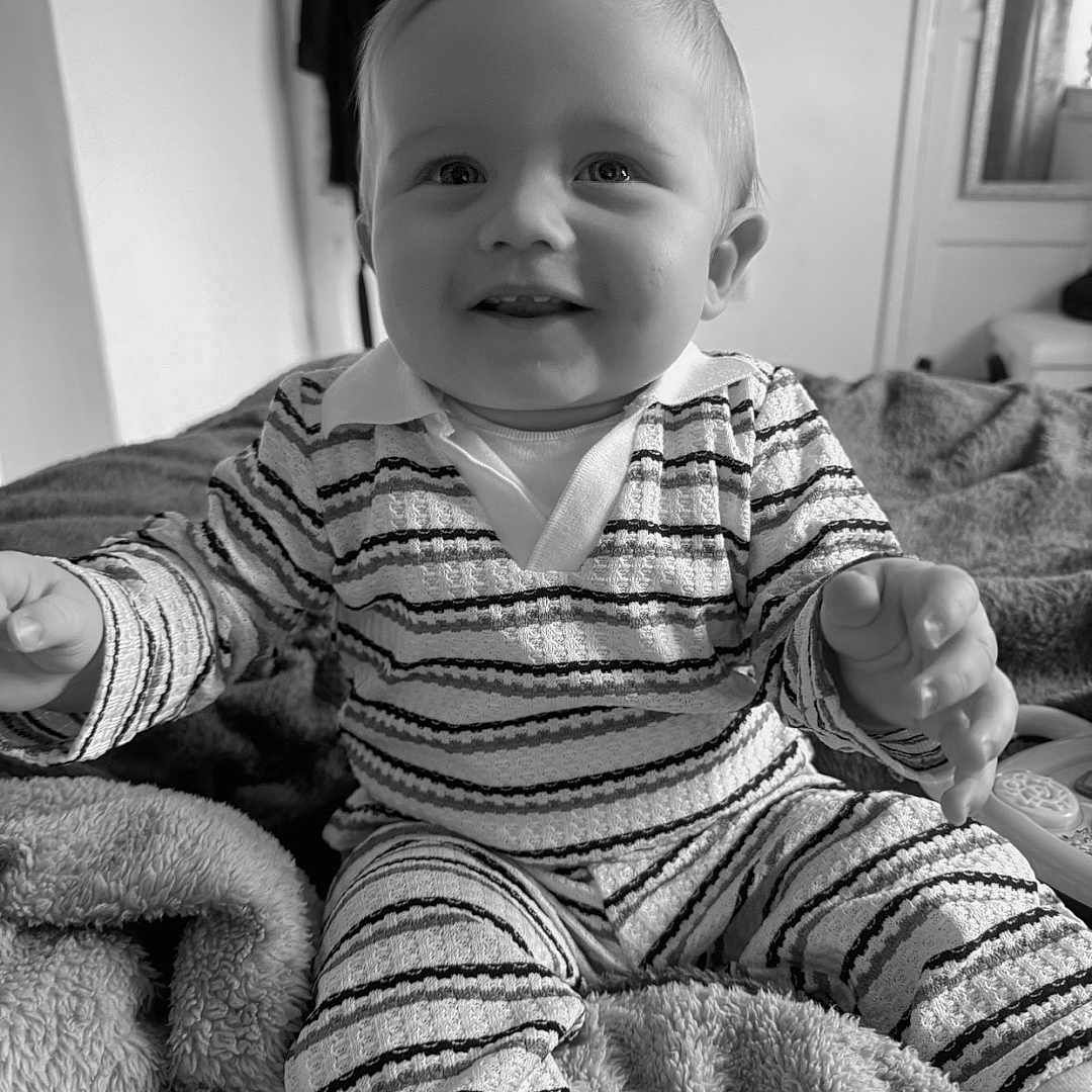 Tommy-Lee joined the competition — help win amazing prizes! baby, black_and_white, blanket, child, cozy, cute, furniture, happy, home, indoor, infant, monochrome, pajamas, person, portrait, relaxed, sitting, smiling, soft_texture, striped_clothing