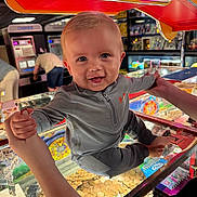 Tommy-Lee is registered to the contest to win money with this photo: toddler, child, arcade, coin_pusher, game, smile, happy, playful, hands, holding, colorful, lighting, indoor, entertainment, clothing, person, face, toy, amusement, fun