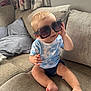 Tommy-Lee joined the competition — help win amazing prizes! baby, child, sunglasses, couch, sofa, curtains, tie_dye_shirt, blue_shirt, shorts, barefoot, indoor, window, pillow, smiling, cute, person, infant, home, seated, fashion