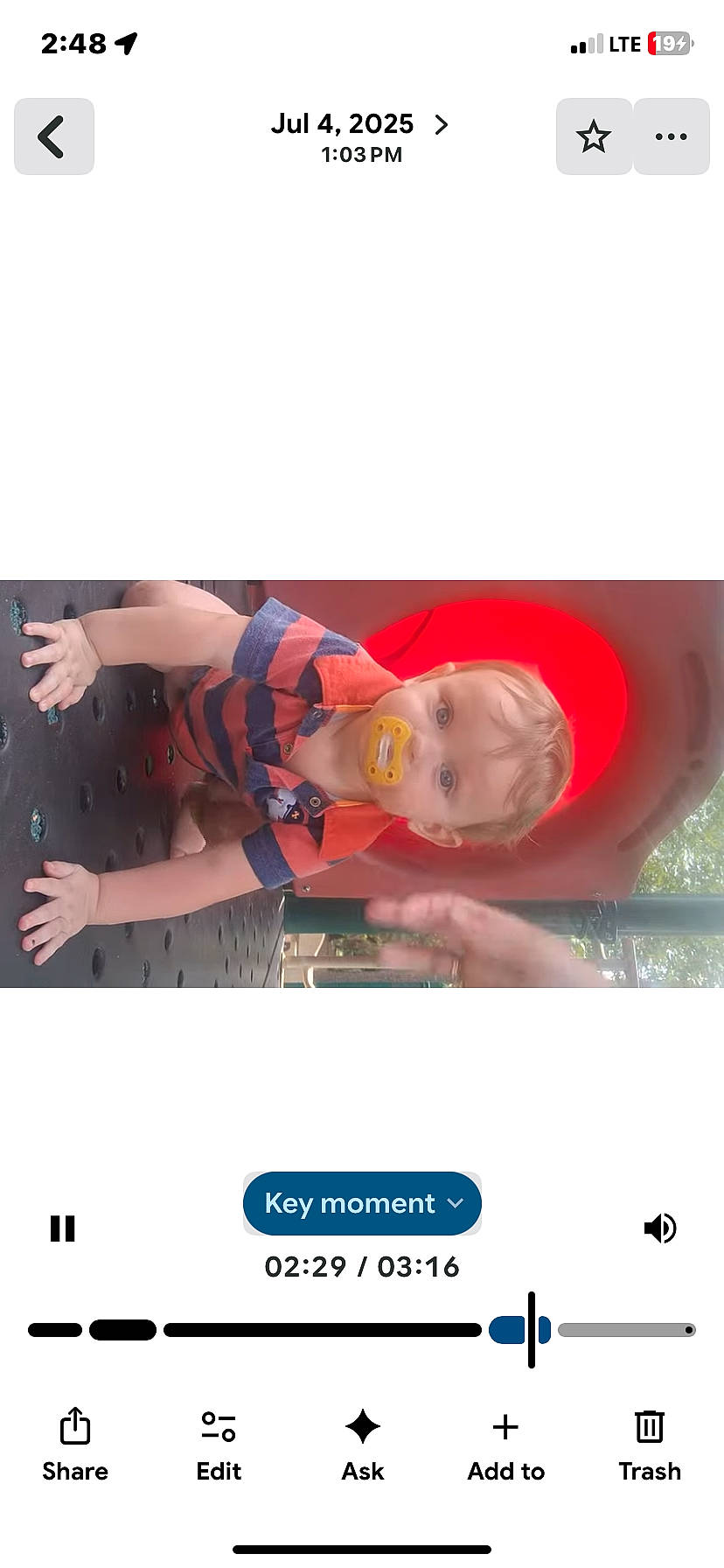 baby, child, crawling, curious_expression, greenery, hands, metal_structure, outdoor, pacifier, parent_hand, pause_icon, platform, play_equipment, playground, portrait, slide_tunnel, striped_shirt, timestamp, ui_elements, video_overlay