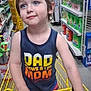 blue_eyes, casual_clothing, child, colorful_shorts, grocery_store, happy, household_products, indoor, person, portrait, retail, shelves, shopping, shopping_cart, smiling, store_aisle, tank_top, tousled_hair, yellow_cart, young_child