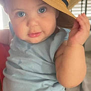 Sabina is registered to the contest to win money with this photo: baby, child, hat, straw_hat, cute, indoor, blue_clothing, face, eyes, hand, curious, smiling_hat, person, portrait, sitting, young_child, infant, plush_hat, expression, closeup