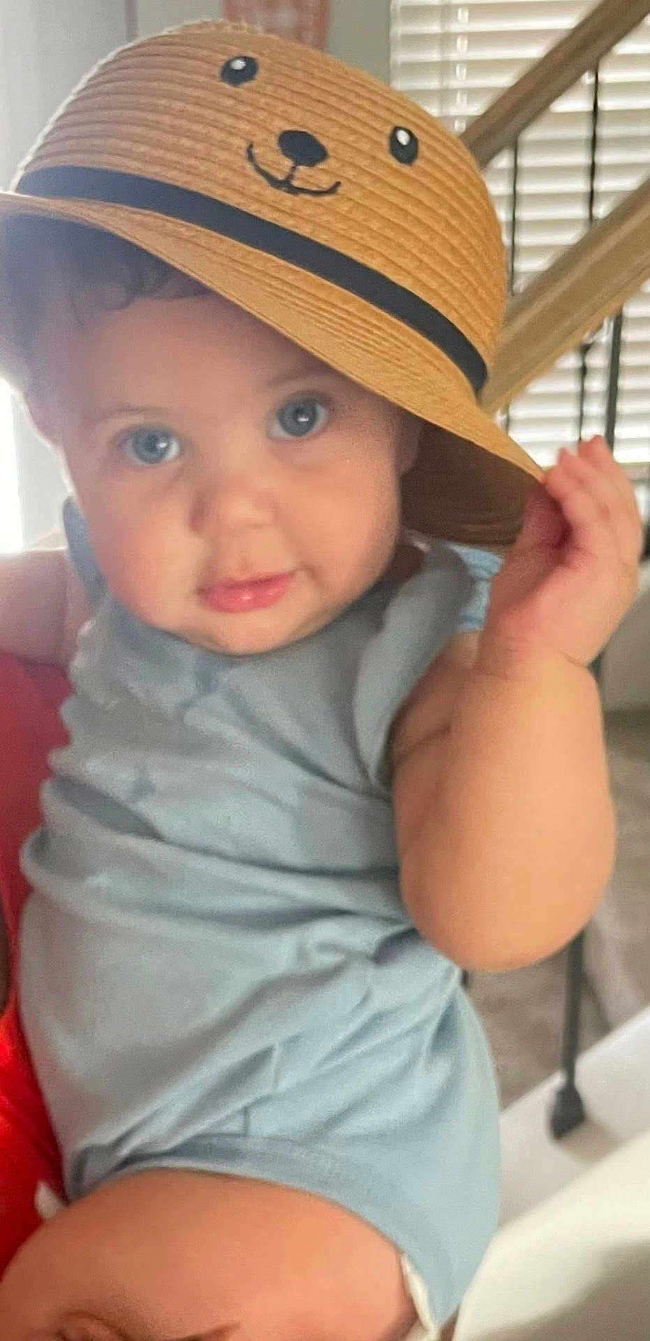 Sabina is registered to the contest to win money with this photo: baby, child, hat, straw_hat, cute, indoor, blue_clothing, face, eyes, hand, curious, smiling_hat, person, portrait, sitting, young_child, infant, plush_hat, expression, closeup