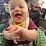 baby, child, messy_face, food, hands, high_chair, bib, clothing, indoor, smiling, happy, infant, seat_belt, green_cushion, face, tongue_out, person, cute, playful, feeding_time