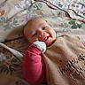 baby, smile, bed, blanket, bib, glove, floral_pattern, happy, infant, person, portrait, sleepwear, cozy, soft, cute, child, lying_down, indoors, fabric, resting