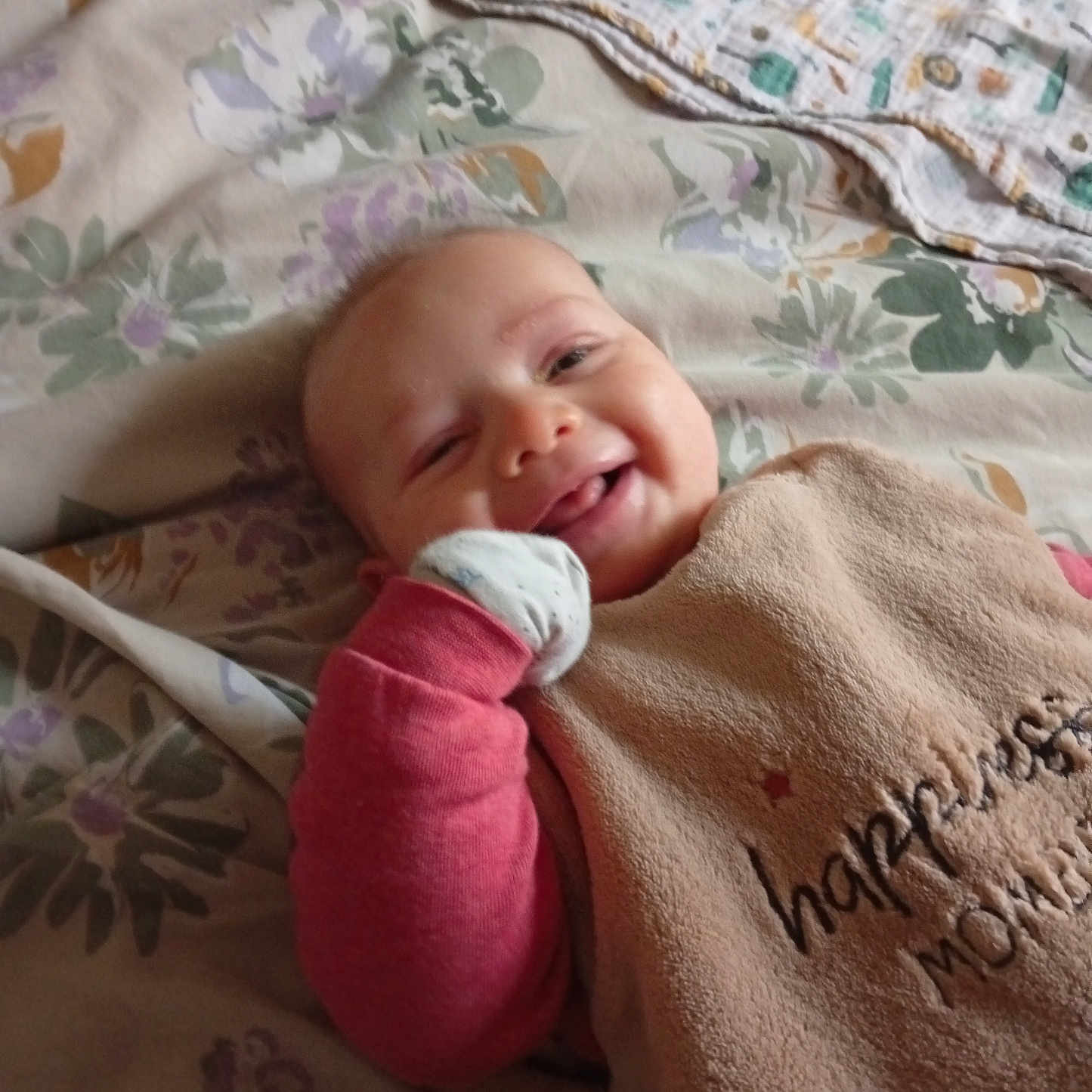 Eli participe au concours pour gagner de l'argent avec cette photo : baby, smile, bed, blanket, bib, glove, floral_pattern, happy, infant, person, portrait, sleepwear, cozy, soft, cute, child, lying_down, indoors, fabric, resting