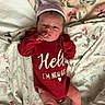 newborn, baby, infant, child, portrait, lying_down, blanket, floral, clothing, red_outfit, striped_hat, socks, bed, indoors, face, eyes_open, hand, sleepwear, newborn_photo, cozy