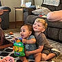 child, children, baby, toy, hug, smile, living_room, carpet, couch, pillow, lamp, table, footwear, shirt, happy, play, indoor, floor, furniture, cute