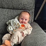 Emme joined the competition — help win amazing prizes! baby, child, infant, smile, pajamas, blanket, toy, couch, furniture, indoors, happy, cute, face, cozy, clothing, socks, person, home, relaxing, portrait