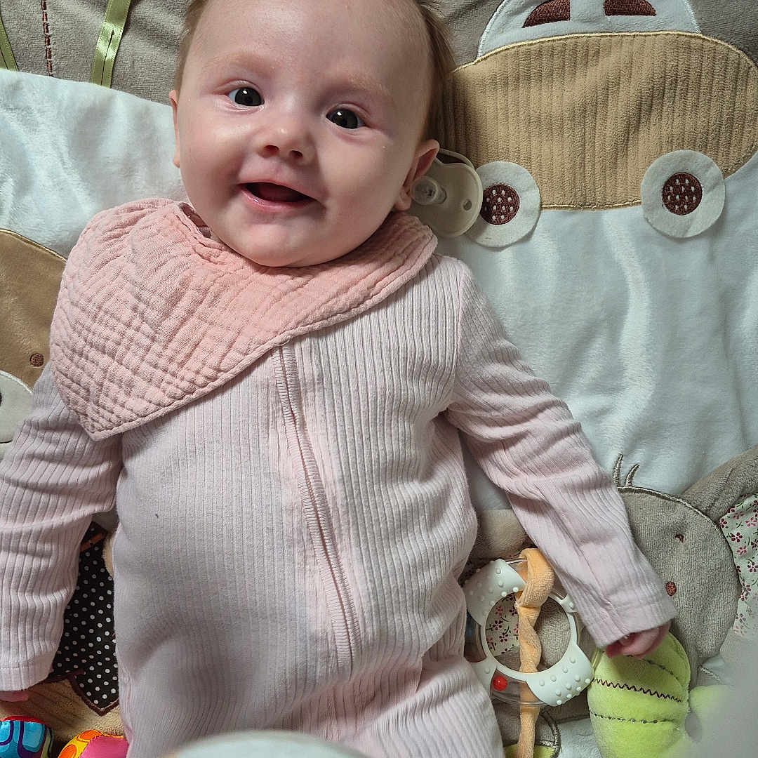 Emme joined the competition — help win amazing prizes! baby, bib, child, closeup, colorful_toys, cute, fabric, face, giraffe_toy, happy, indoors, infant, lying_down, pattern, person, pink_onesie, playmat, smiling, soft_toys, young_child