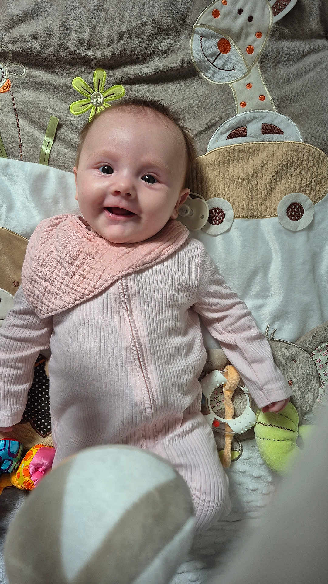 Emme joined the competition — help win amazing prizes! baby, infant, smiling, pink_onesie, bib, playmat, giraffe_toy, soft_toys, colorful_toys, lying_down, happy, face, cute, child, indoors, fabric, pattern, closeup, person, young_child