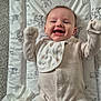Emme is registered to the contest to win money with this photo: baby, infant, smile, happy, lying_down, onesie, bib, changing_pad, patterned, tissue, carpet, indoor, cute, young_child, raised_arms, face, cheerful, soft_lighting, expression, clothing