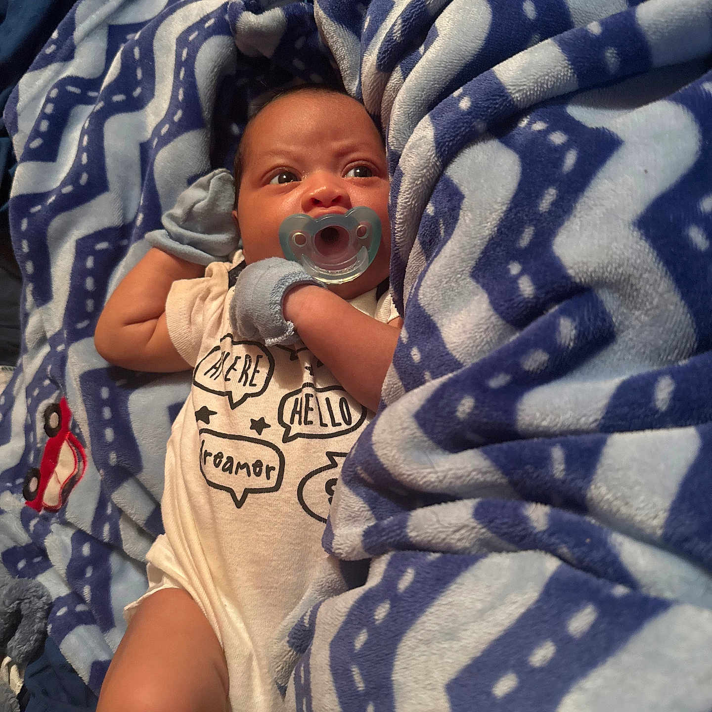Jakarri is registered to the contest to win money with this photo: baby, infant, child, pacifier, blanket, blue_blanket, onesie, speech_bubbles, lying_down, wide_eyed, portrait, indoor, cozy, soft_fabric, bed, clothing, face, hands, arms, photography
