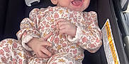 Montana is registered to the contest to win money with this photo: baby, infant, smiling, laughing, floral_clothing, onesie, stroller, child, cute, happy, sitting, person, face, hand, foot, fabric, seat, black, comfort, joy