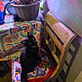 cat, black_cat, chair, cushion, wooden_chair, indoor, potted_plant, tablecloth, colorful, patterned, curious, pet, feline, looking_up, decor, home, cozy, plant, animal, domestic
