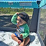 Ozias is registered to the contest to win money with this photo: baby, barefoot, blanket, cap, cartoon_character, casual, child, curious, grass, green_shirt, hat, mesh, nature, outdoor, playpen, portrait, shadow, sitting, sunlight, toddler
