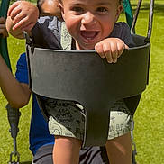 Ozias is registered to the contest to win money with this photo: baby, child, curly_hair, footwear, fun, grass, greenery, happy, holding, nature, outdoor, park, person, play, playground, smiling, summer, sunlight, swing, toddler