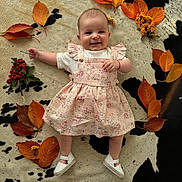 Emilia is registered to the contest to win money with this photo: baby, infant, smiling, dress, white_shoes, autumn_leaves, berries, cowhide_rug, floor, laying_down, child, happy, cute, nature_elements, indoor, portrait, seasonal, fall_colors, person, young_child