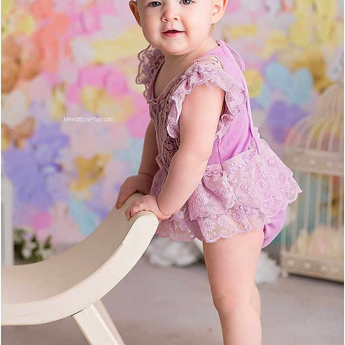Nato is registered to the contest to win money with this photo: baby, barefoot, chair, child, cute, fashion, floral, girl, headband, indoor, lace, pastel_background, person, portrait, purple_outfit, smiling, soft_lighting, standing, studio_photo, young_child