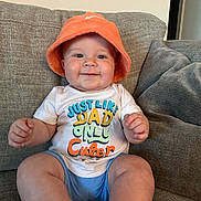 Daxton joined the competition — help win amazing prizes! baby, child, infant, hat, orange_hat, tshirt, sitting, couch, gray_couch, smiling, happy, indoor, furniture, cute, chubby, clothing, face, person, home, portrait