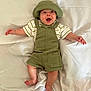 arms_outstretched, baby, barefoot, child, clothing, cute, expression, fabric, green_hat, green_overalls, happy, headwear, indoors, infant, lying_down, person, portrait, smiling, striped_shirt, white_sheet