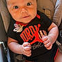 baby, infant, child, car_seat, onesie, black_clothing, red_clothing, pacifier, cute, wide_eyes, hands, indoor, seatbelt, portrait, human, young_child, soft_lighting, clothing, baby_fashion, expression