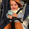 baby, baby_bib, cap, car_seat, child, clothing, face, hand, happy, indoor, infant, orange_pants, pacifier, person, seatbelt, smiling, stroller, teething_toy, toy, water_bottle