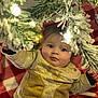 Cody is registered to the contest to win money with this photo: baby, child, christmas_tree, ornament, gold_ball, blanket, red_and_white, pine_branch, snowy, holiday, curious, indoor, cozy, cute, sweater, infant, face, expression, hand, festive