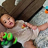 baby, child, toy, car, green, wheels, shirt, winnie_the_pooh, beige, carpet, floor, couch, brown, sitting, curious, indoor, footwear, person, cute, playful