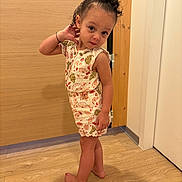 Louna participe au concours pour gagner de l'argent avec cette photo : barefoot, casual, child, clothing, curly_hair, cute, door, feet, floor, floral_pattern, indoor, person, portrait, pose, romper, standing, toddler, wall, wooden_floor, young_child