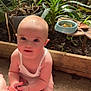 Maddison is registered to the contest to win money with this photo: baby, child, infant, sitting, hand_holding, white_clothing, garden, plants, pot_plants, greenery, sunlight, outdoor, curious, bright_eyes, cute, skin, floor, person, tattoo, natural_light