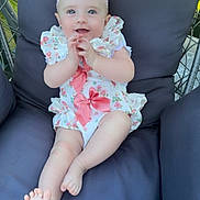 Maddison is registered to the contest to win money with this photo: baby, child, smiling, blue_eyes, pink_bow, headband, floral_outfit, cushioned_chair, outdoor, grass, happy, person, infant, cute, sitting, foot, hand, portrait, comfortable, sunlight
