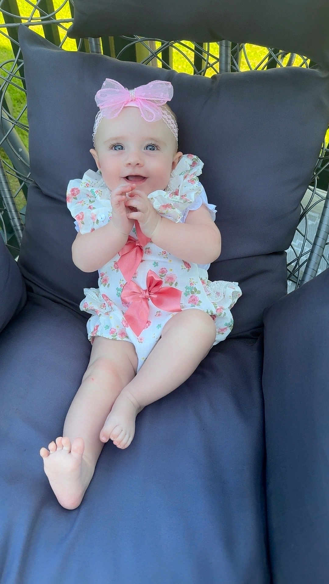 Maddison is registered to the contest to win money with this photo: baby, child, smiling, blue_eyes, pink_bow, headband, floral_outfit, cushioned_chair, outdoor, grass, happy, person, infant, cute, sitting, foot, hand, portrait, comfortable, sunlight