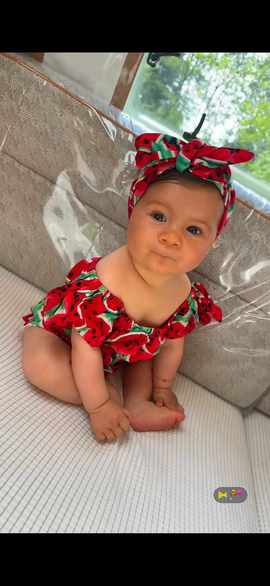 Syanna participe au concours pour gagner de l'argent avec cette photo : baby, child, infant, headband, red_clothing, watermelon_pattern, sitting, curious_expression, indoors, window, greenery, soft_surface, textured_background, cute, portrait, skin, face, hands, feet, natural_light
