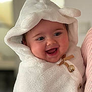 Maëlya a rejoint le concours — aidez-le/la à gagner de superbes lots ! baby, infant, hood, towel, smile, chubby_cheeks, closeup, portrait, cozy, blanket, button, bow, eyes, mouth, person, parent_arm, cuddly, indoors, soft_texture, happy