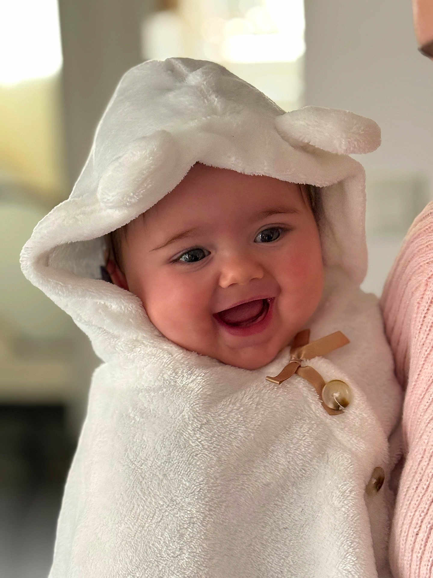 Maëlya a rejoint le concours — aidez-le/la à gagner de superbes lots ! baby, infant, hood, towel, smile, chubby_cheeks, closeup, portrait, cozy, blanket, button, bow, eyes, mouth, person, parent_arm, cuddly, indoors, soft_texture, happy
