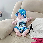 Kamden is registered to the contest to win money with this photo: baby, child, smiling, hat, blue, tropical, outfit, sitting, couch, beige, blanket, towel, indoor, happy, person, infant, clothing, face, cute, relaxing