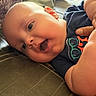 Mathéo a rejoint le concours — aidez-le/la à gagner de superbes lots ! baby, infant, smiling, happy, face, mouth_open, blue_shirt, glasses_print, hand, couch, pillow, blanket, indoor, closeup, skin, head, ear, child, person, casual