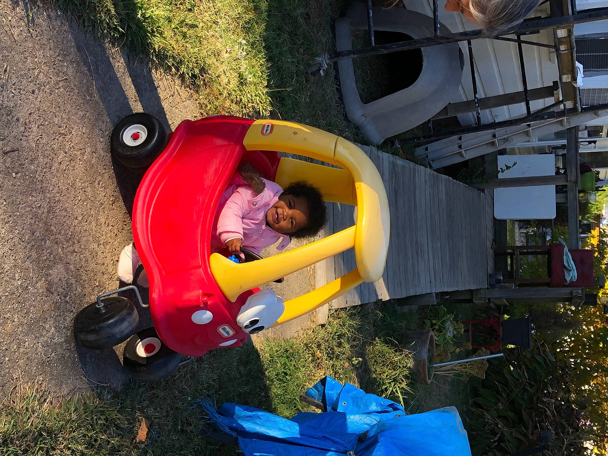 Brinleigh is registered to the contest to win money with this photo: asphalt, automotive_exterior, automotive_tire, automotive_wheel_system, blue, fun, grass, green, leisure, motor_vehicle, outdoor_play_equipment, person, plant, recreation, tire, toddler, tree, vehicle, vehicle_door, wheel