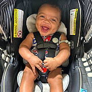 Madden is registered to the contest to win money with this photo: baby, car_seat, smiling, happy, infant, child, seatbelt, safety, black, striped, warning_label, clothing, hand, legs, indoor, cute, portrait, person, seat, bright
