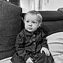 toddler, child, face, denim_dress, sitting, couch, blanket, indoor, portrait, black_and_white, clothing, young_child, expression, buttoned_shirt, hand, hair, cozy, furniture, person, home