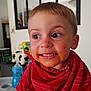 toddler, child, messy_face, red_bib, high_chair, indoor, playful_expression, food_stains, short_hair, big_eyes, home, toy, table, furniture, person, cute, smiling, face, clothing, baby