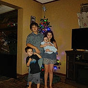 Wyatt James is registered to the contest to win money with this photo: child, children, christmas_tree, holiday, indoor, living_room, family, decorations, floor, barefoot, smile, baby, sibling, television, furniture, wood_floor, curtain, casual_clothing, portrait, group