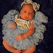 Juliana is registered to the contest to win money with this photo: baby, infant, blue_dress, headband, ruffles, blanket, lying_down, cute, newborn, soft_lighting, infant_clothing, skin, foot, hand, portrait, indoors, person, baby_fashion, baby_girl, sleepwear