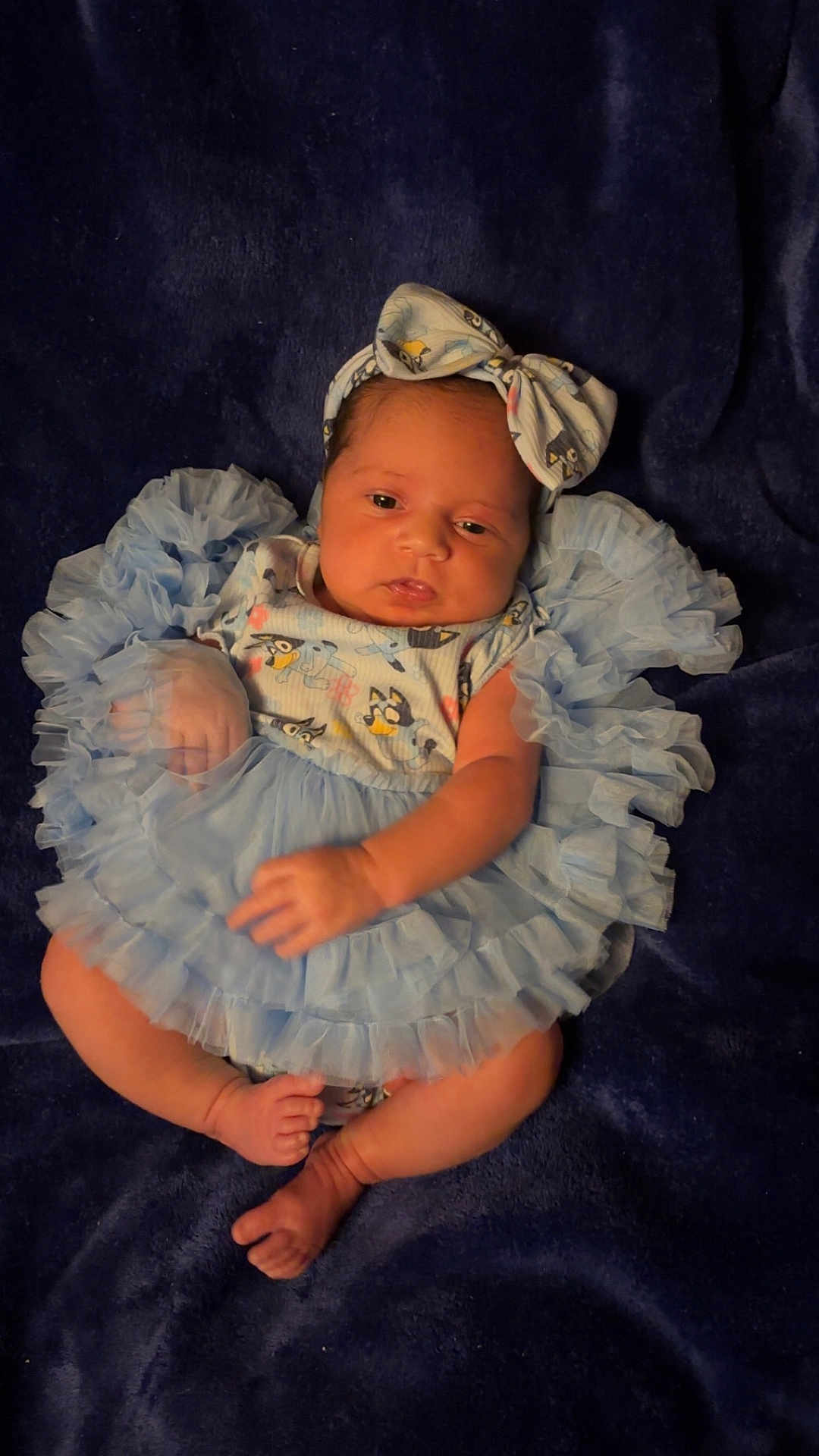 Juliana is registered to the contest to win money with this photo: baby, infant, blue_dress, headband, ruffles, blanket, lying_down, cute, newborn, soft_lighting, infant_clothing, skin, foot, hand, portrait, indoors, person, baby_fashion, baby_girl, sleepwear