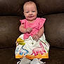 baby, child, smile, pink_top, dinosaur_skirt, white_shoes, couch, brown_couch, sitting, happy, infant, cute, portrait, indoor, clothing, footwear, person, young_child, fashion, colorful
