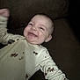 baby, smiling, onesie, couch, happy, infant, child, clothing, face, person, indoor, cute, young, baby_gesture, expression, baby_sleepwear, relaxed, cheerful, baby_fashion, baby_boy
