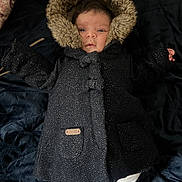 Ilef participe au concours pour gagner de l'argent avec cette photo : baby, infant, coat, hood, fur, black_coat, blanket, white_pants, lying_down, indoor, face, person, cute, warm_clothing, child, newborn, sleepwear, portrait, baby_clothes, soft