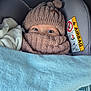 baby, child, hat, scarf, blanket, car_seat, airbag_warning, blue_blanket, cozy, warm_clothing, wide_eyes, winter, snug, infant, portrait, close_up, indoor, soft_texture, cute, wrapped_up